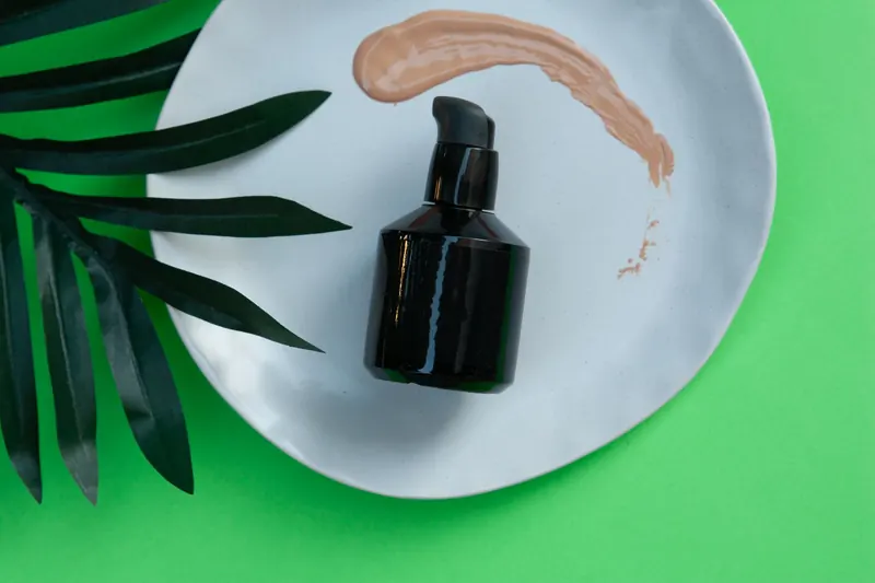 Black skincare pump bottle on a white plate with green leaf and makeup smear