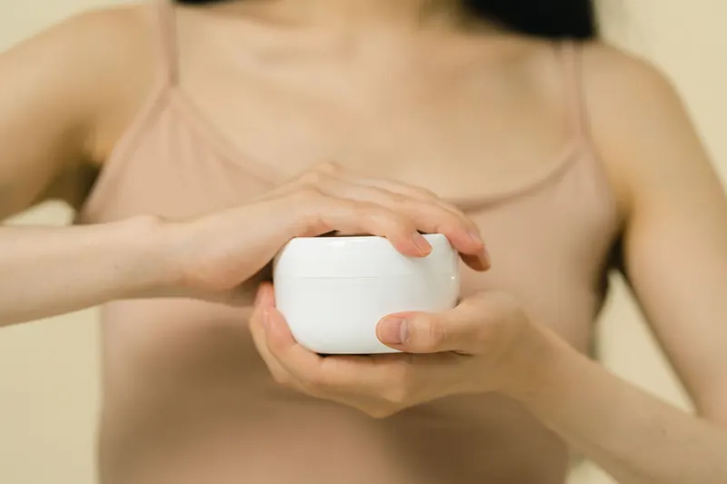 Close-up of a woman applying moisturizer with a focus on her hands and the cream container
