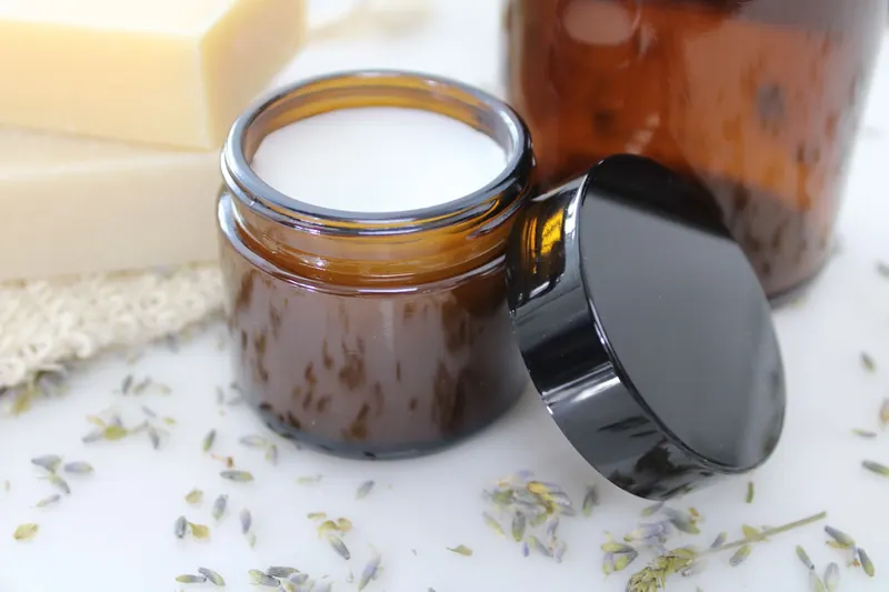 Delicate natural cream in amber glass jar, surrounded by lavender and beeswax, perfect for skincare routines