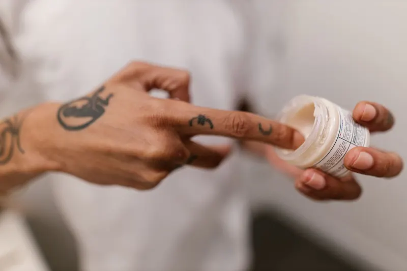Close-up of a tattooed hand applying cream, emphasizing skincare and personal grooming