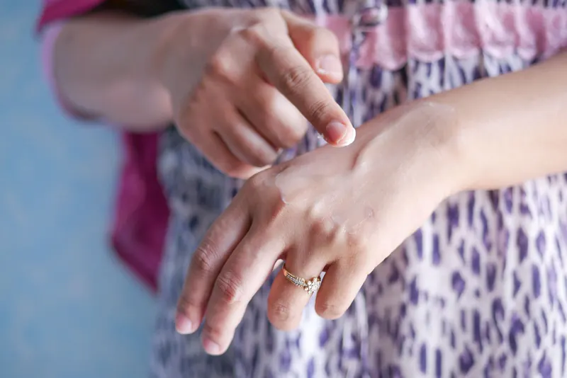A woman applies skincare cream on her hand, highlighting moisturizing routine