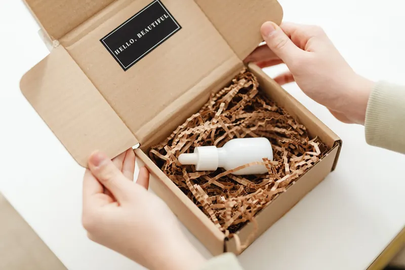 Hands opening a package with a skincare dropper bottle in protective packaging