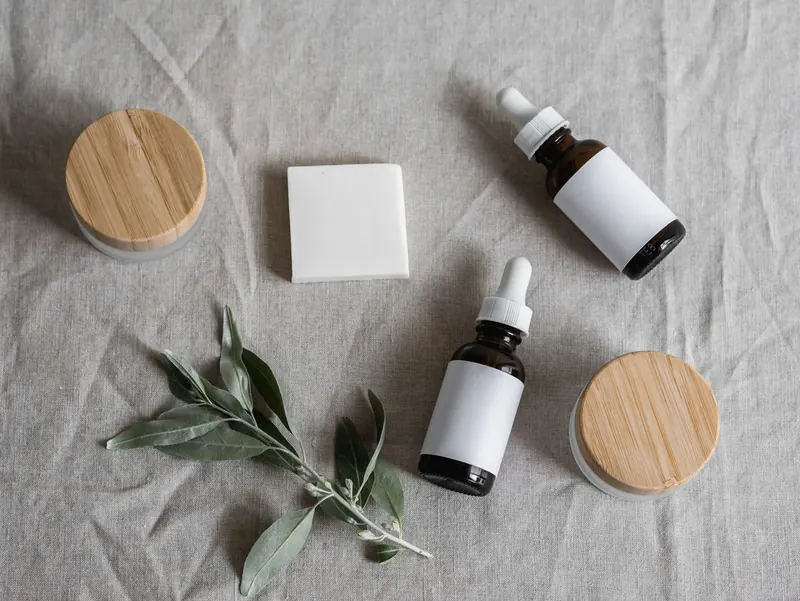 Top view of skincare products with a natural theme, featuring bottles, jars, and a plant on linen cloth