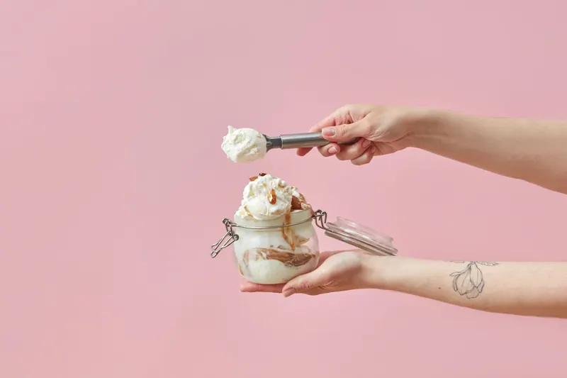 Delicious caramel ice cream in a glass jar against a pastel pink background, scooped for a sweet treat