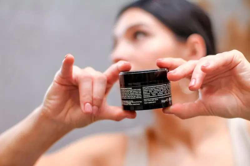 Woman holding a cosmetic cream product, showcasing beauty and skincare focus