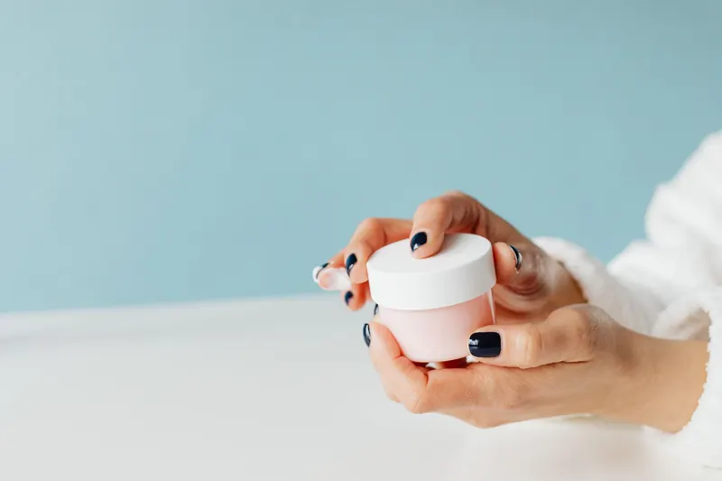 Close-up image of hands holding a skincare cream jar, focusing on beauty and self-care products