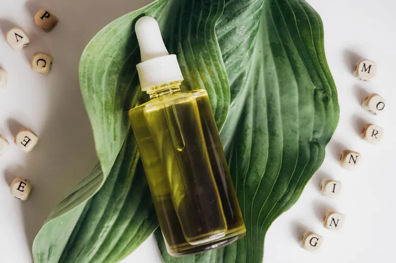 A bottle of natural skincare oil placed on green leaves with letter blocks spelling out 'morning'