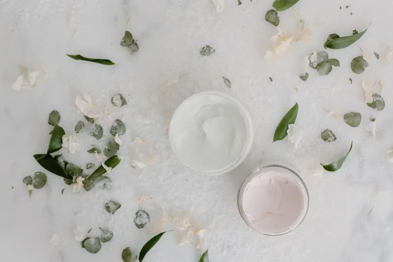 Flat lay of cosmetic cream jars surrounded by natural leaves and petals, perfect for beauty product promotions
