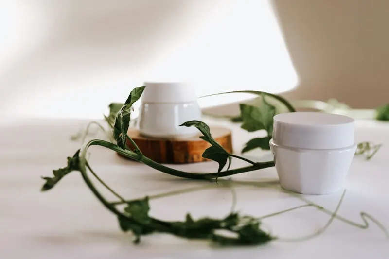 White cream jars with green leaves, elegantly arranged in a minimalist setting