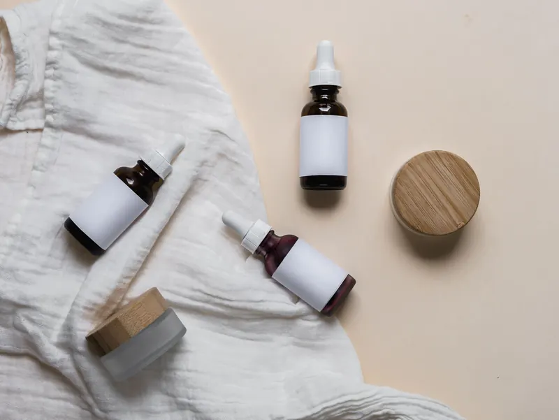 Elegant glass skincare bottles with labels on a textured fabric, perfect for cosmetic branding and product display