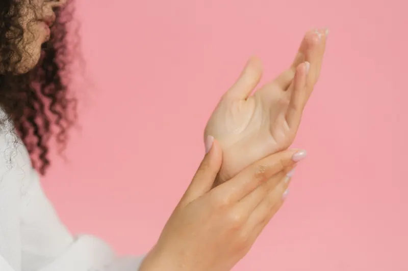 Close-up of hands applying cream on a pink backdrop. Perfect for skincare themes