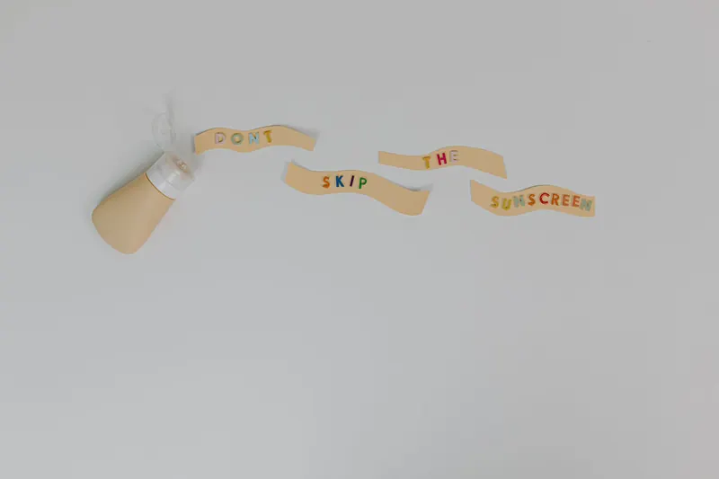 Sunscreen bottle and creative text 'Don't Skip the Sunscreen' on white background, promoting skincare and cancer prevention