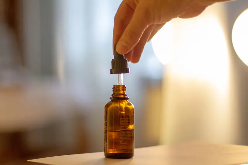 A hand carefully holding a dropper bottle with a blurred background, showcasing skincare serum