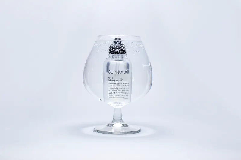 A luxury serum bottle submerged in a large wine glass filled with water, showcasing purity and elegance