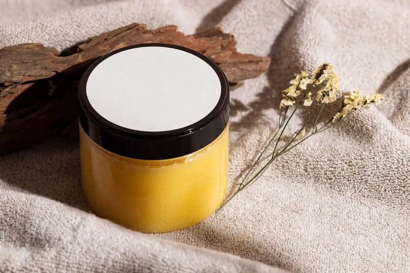 Jar of yellow skincare cream on a towel with wood and dried flowers, ideal for spa themes