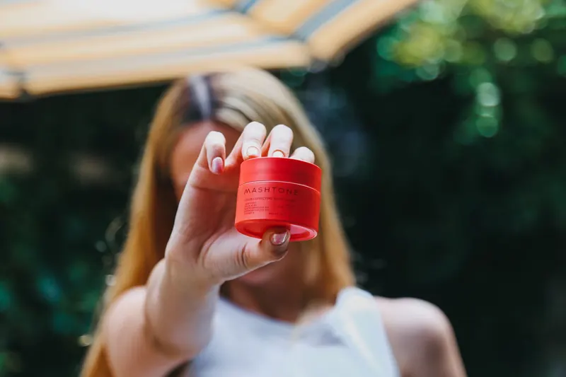 Close-up of a woman holding a Mashtone skincare cream jar in a natural outdoor setting